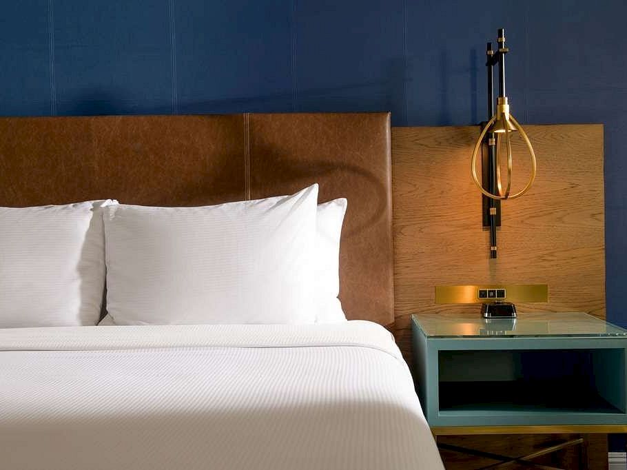 A modern hotel room with a bed, bedside table, and a brass pendant lamp casting light.