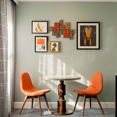 A bright room with an orange chair set, small round table, and framed wall art above a gray-and-white rug.