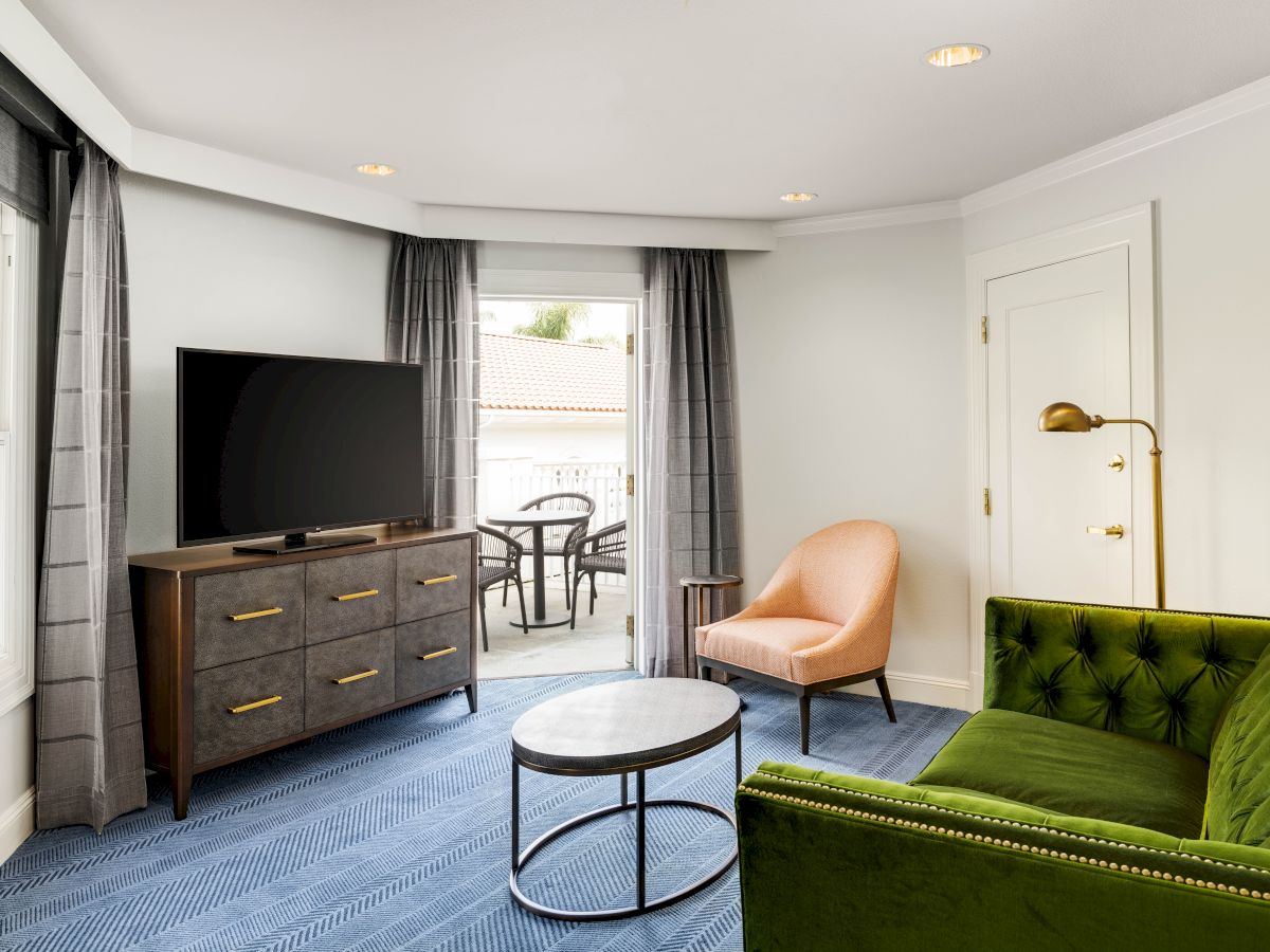 Bright living room with a flat-screen TV, gray curtains, green sofa, coffee table, and a window and door to a balcony.