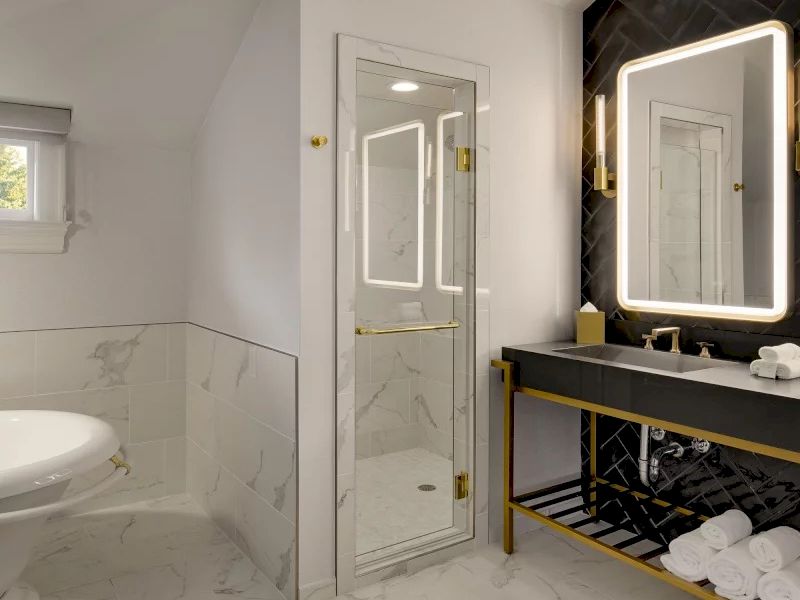A luxurious bathroom with a marble floor and walls, a glass-door shower, a modern vanity with a backlit mirror, and neatly rolled towels.