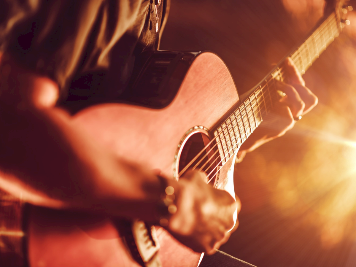Close-up of an electric guitar being played onstage, lit by warm concert lights and smoky haze.