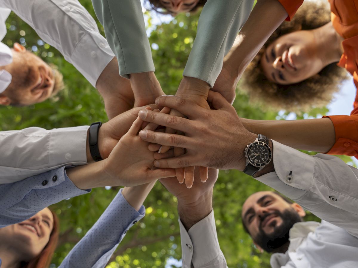 A group of people outdoors raises their hands together, clasping in teamwork and celebration.