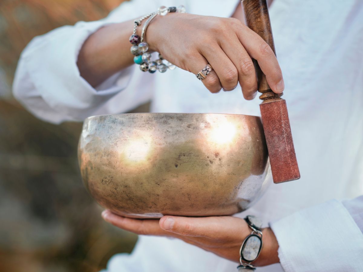 A person&rsquo;s bejeweled hand holds a shiny copper kettle pot outdoors, lifting it carefully for use.