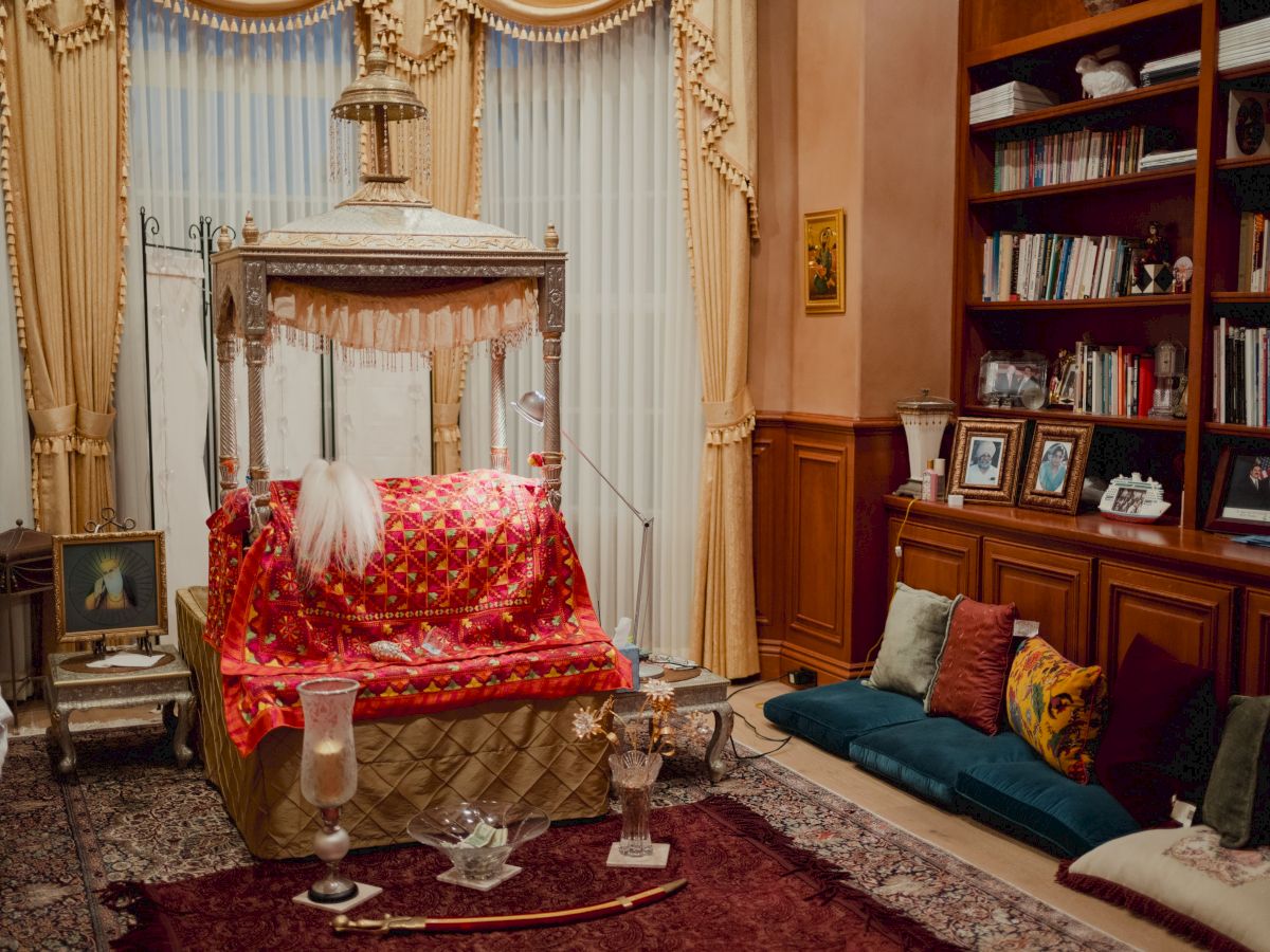 An elegant lounge with a gold canopy bed draped in bright fabric, ornate curtains, and a wooden bookshelf wall.