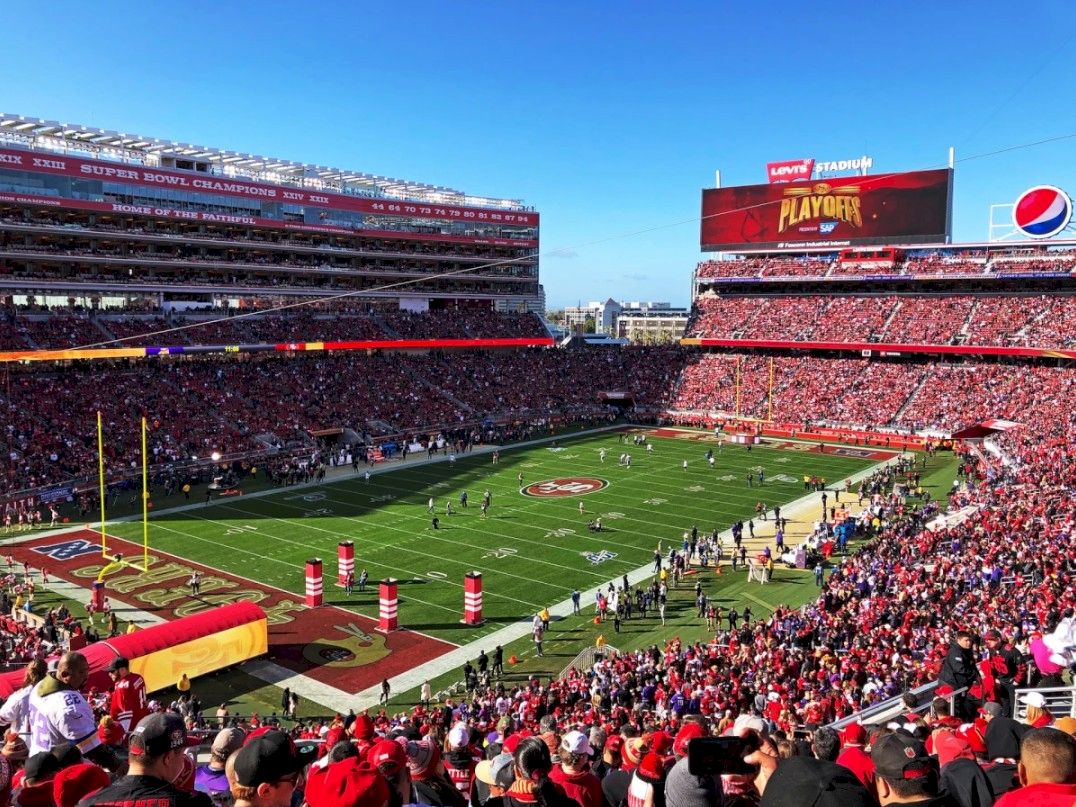 A packed Levi&rsquo;s Stadium football game with fans in red cheering on the field during the playoff.