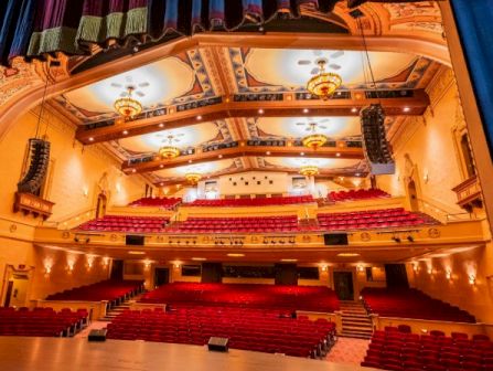 An ornate theater interior with red seats, gilded balconies, and chandeliers under a decorative ceiling.
