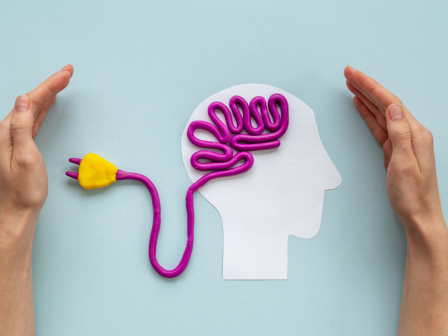 A cutout head silhouette with purple &ldquo;brain&rdquo; squiggle, a yellow lightbulb on a purple cord, and hands framing the scene.