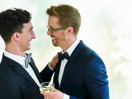 Two men in suits smile and toast while holding wine glasses during a friendly moment.