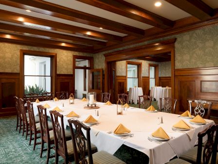 A formal banquet room with long tables set with white linens, gold napkins, candles, and ornate chairs under warm ceiling lights.