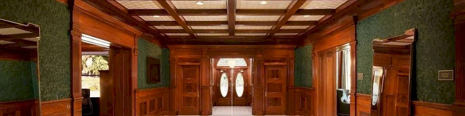 A spacious room with green wallpaper and dark wooden trim, featuring a vaulted wooden ceiling and double doors with oval lights.
