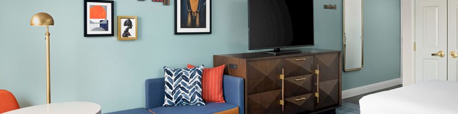 A modern blue-walled room with a sofa bench, framed art, a flat-screen TV, and a standing mirror.