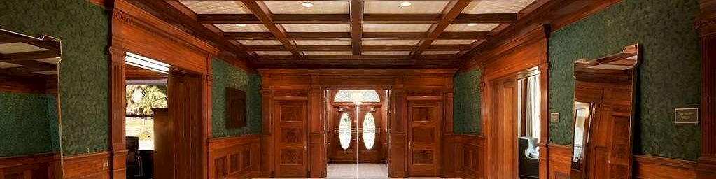 An elegant hallway with dark wooden ceiling beams, green patterned walls, and green bench seats flanked by mirrors.