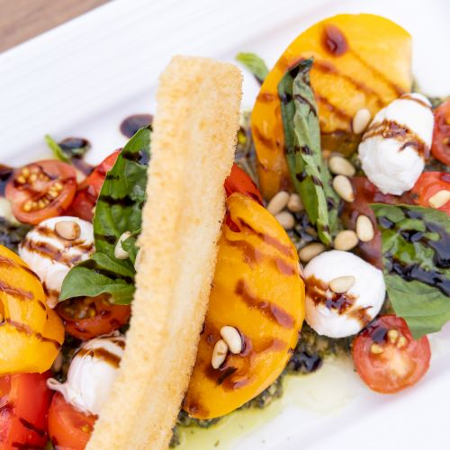 A veggie salad with tomatoes, greens, pine nuts, mozzarella, and a golden breadstick on a white plate.
