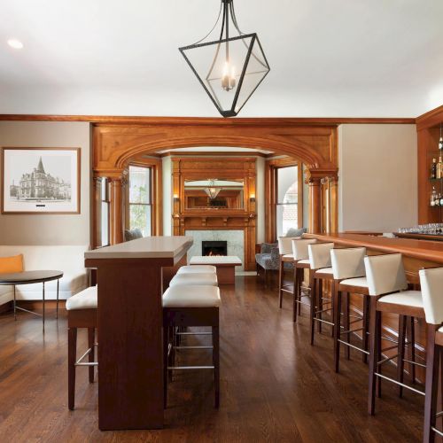 A stylish bar interior with wooden surfaces, high stools, a long counter, and a warm, inviting seating area.