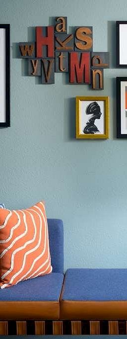 A stylish living room corner with a blue sofa, colorful cushions, wall art gallery, a wooden floor lamp, and a minty-green wall.