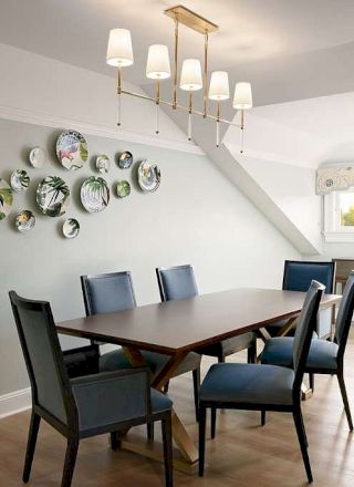 A modern dining room with a wooden table, blue chairs, a hanging chandelier, and decorative wall plates.